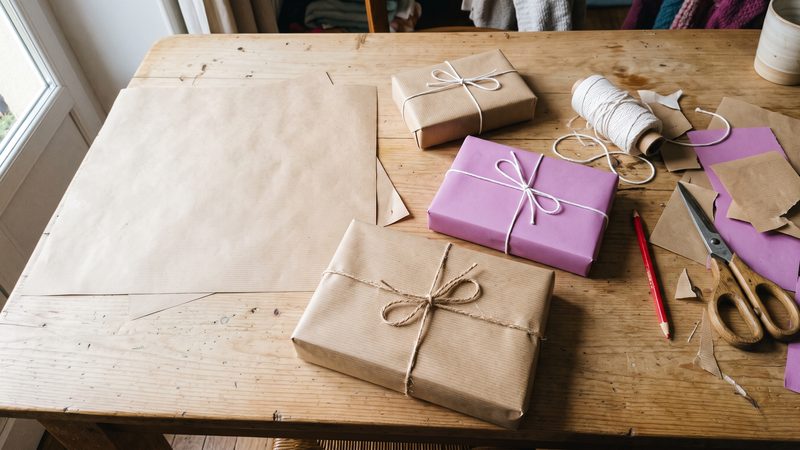 Trois paquets cadeaux en papier kraft et papier orchidée, ficelle blanche, sur une table en bois clair