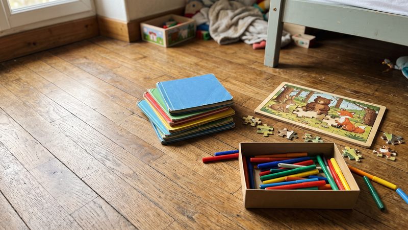 Pile de livres d'enfants, puzzle à moitié fait et boîte de feutres sur un parquet usé